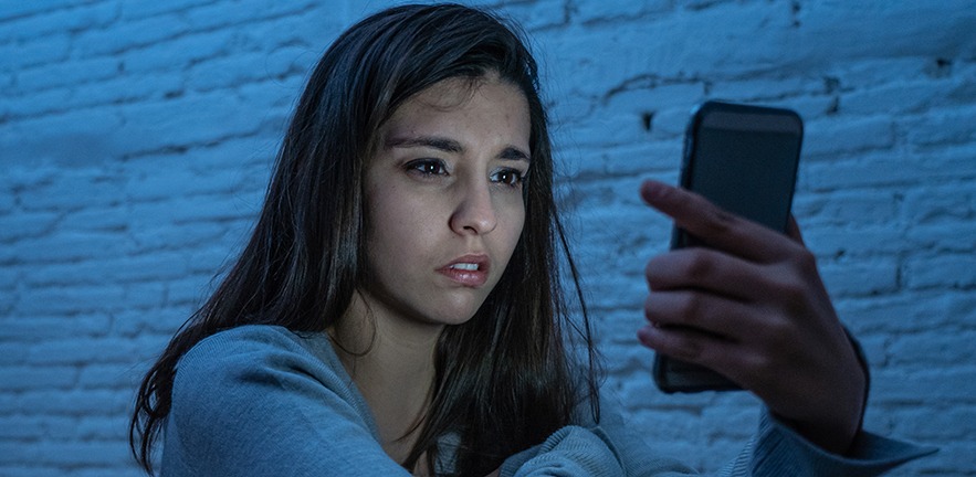 Portrait of sad scared young woman on mobile smart phone on the floor at night stressed and worried suffering cyber bullying harassment.